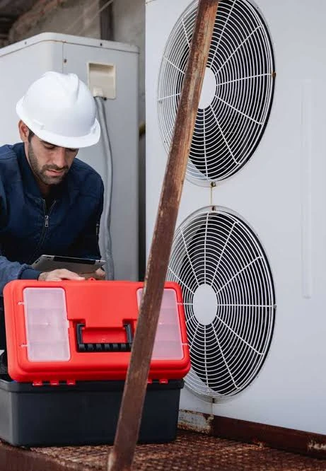 Technician checking outdoor HVAC equipment beside a red toolbox