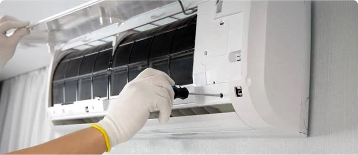 Gloved hands servicing the filter compartment of a wall-mounted air conditioner
